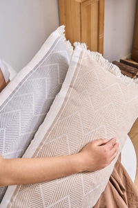 Detail of jacquard geometric cushions with fringes in grey and beige tones