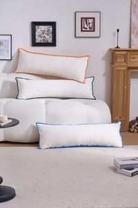 Detailed view of white rectangular bolster pillows with colorful pom-pom fringe edges
