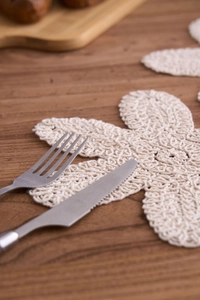 Nahaufnahme eines handgehäkelten Baumwoll-Untersetzers in Blumenform in Creme