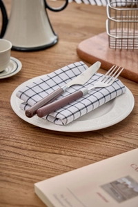 Close-up of brown handle cutlery set with black plaid napkin on white ceramic plate