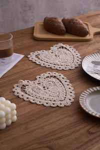 Detail of two handmade heart-shaped crochet coasters on a rustic wooden table setup