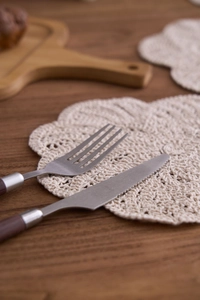 Detail of a handmade beige crochet coaster set under stainless steel cutlery on wood