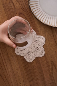 Detailed macro view of handmade cotton crochet coaster with textured floral pattern on wood