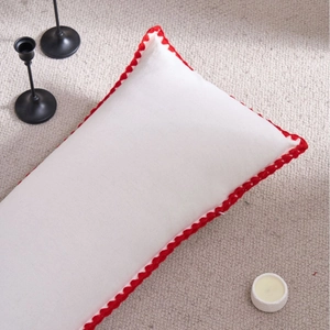 White rectangle pillow with red scalloped trim on beige textured rug background