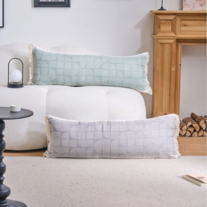 Long jacquard lumbar pillow with geometric arch patterns and decorative tassels on a sofa