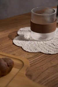 Close-up of a handmade crochet cotton coaster with a glass tea cup on a wooden table