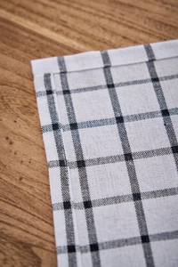 Detailed view of checkered cotton linen napkin stitching on a wooden table surface