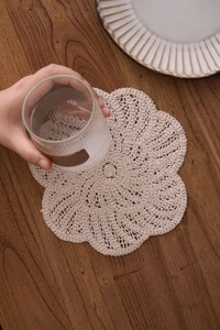 Macro detail of a cream handmade crochet floral coaster on a dark wood table
