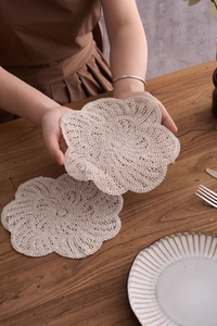 Detail of handmade crocheted cotton flower coaster with scalloped edges on a wooden table