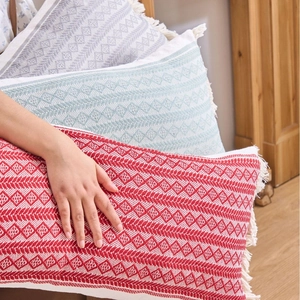 Coussin tissé géométrique bohème avec pompons en tons rouge, bleu clair et gris