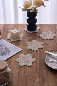 Set of five beige handmade crochet cotton coasters with flower shapes on a wood table
