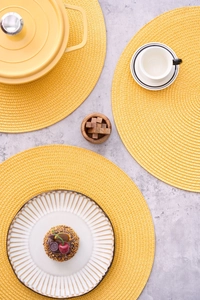 Detailed top view of bright yellow woven round table mats on a grey marble surface