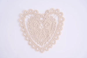 Macro shot of heart-shaped crochet coaster with wave lace edge in creamy beige cotton