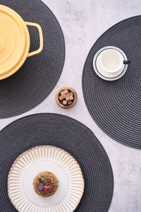 Detailed top view of dark grey round woven table mats with spiral texture on stone surface