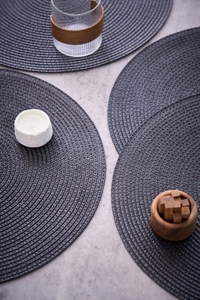 Detailed close-up of dark grey round woven placemats with spiral texture on a stone table