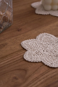 Macro detail of a handmade crochet flower coaster in beige cotton on a dark wooden table