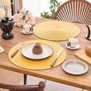 Bright yellow round woven placemat on a wooden dining table with elegant tableware