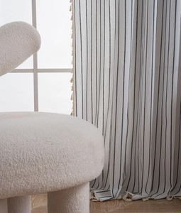 Detail of white linen curtains with black stripes and beige fringe tassels in a bright room