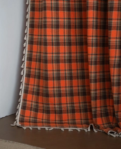 Detail of orange checkered curtain fabric with decorative white fringe tassels