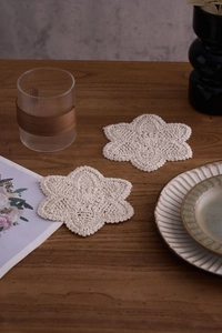 Detail of a handmade cream crochet cotton coaster with floral pattern on a wooden table