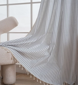 Detail of white striped curtain with handmade tassels on a minimalist beige chair