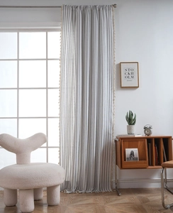 Close-up of black striped cotton linen curtain with beige tassel trim in a modern room