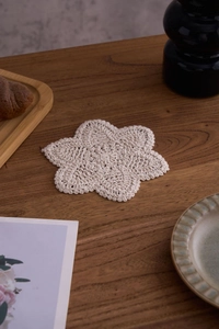 Detailed close-up of a hand-woven cream cotton coaster on a dark wood table surface