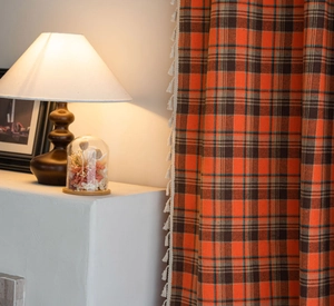 Detail of orange and black plaid curtain with white tassel trim and rustic fabric texture