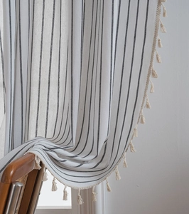 Detail of striped linen curtain fabric with bohemian tassel edges on a wooden chair
