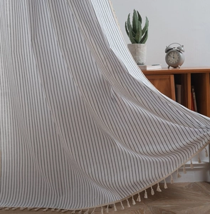 Detail view of cream cotton linen curtain with black stripes and elegant tassel fringe edge