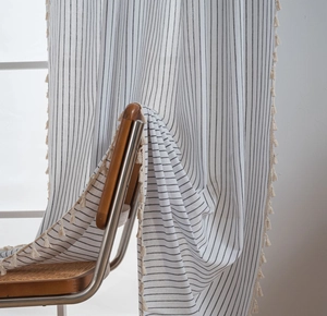 Detail of cream linen curtain with black vertical stripes and decorative tassel edges