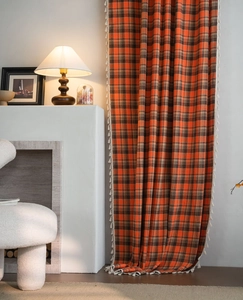 Detail of orange plaid curtains with white fringe tassels in a warm home setting