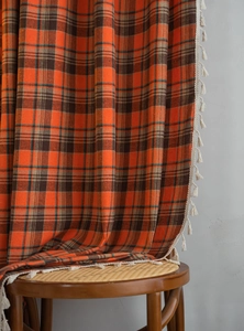 Detailed view of orange checkered fabric with elegant off-white tassel fringe trim