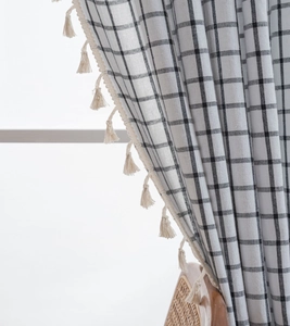 Close-up of black and white checkered linen curtain fabric with cream tassel fringe details