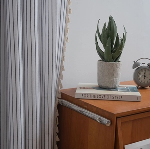 Detail of minimalist striped linen curtain featuring decorative beige fringe tassels