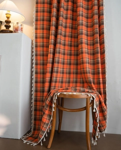 Detail of orange plaid curtains with white tassel fringe on a rustic wooden chair