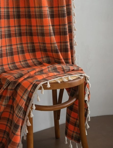 Close-up of orange checkered curtain fabric with white fringe details on a wooden chair
