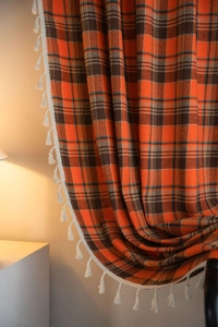 Detail of orange plaid curtains with decorative cream fringe and textured fabric
