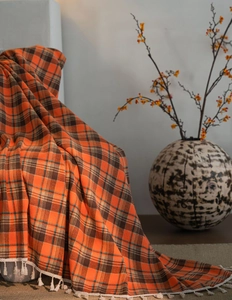 Macro detail of orange and brown plaid fabric texture with white fringed tassels