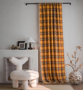 Detailed view of orange plaid curtain featuring white tassel trim and vintage cotton fabric