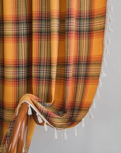 Detail of orange plaid fabric with white tassel fringe draped on a wooden chair back