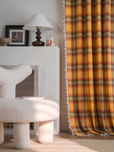 Detail of orange checkered curtain with white tassels in a warm vintage living room