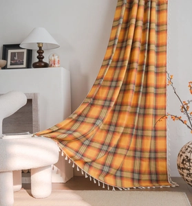 Detailed view of orange checkered french curtain fabric with decorative white fringe tassels