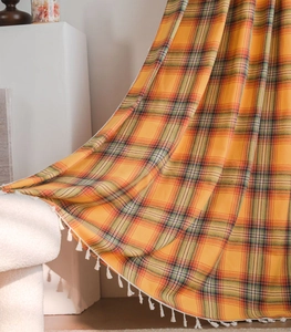 Detail of orange plaid fabric with white tassel trim showing high-quality texture