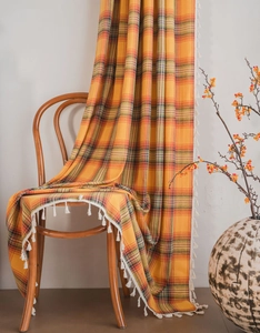 Detail of orange plaid curtain fabric with white tassel trim on a wooden chair