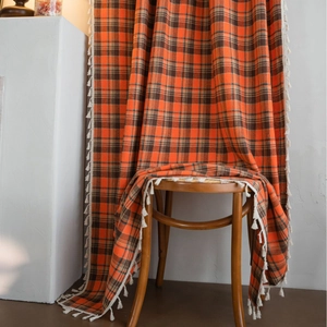 Orange plaid fabric curtain with white tassel trim draped on a vintage wooden chair
