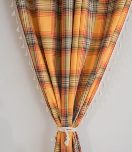 Detail of orange plaid curtains featuring delicate white tassels and a woven tieback rope