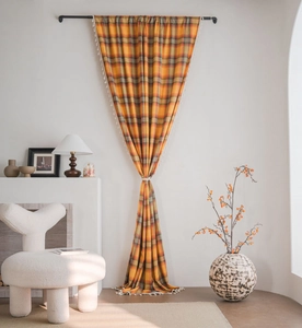 Detail of orange plaid curtains with white tassel trim tied in an hourglass shape