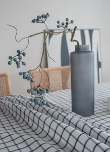 Detail of black and white checkered linen tablecloth with a grey ceramic vase and berries
