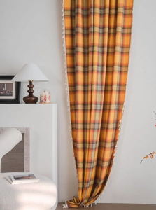Detail of orange plaid curtain fabric featuring white pom-pom fringe in a cozy room
